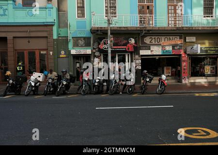 Die Fahrer mit Fast-Food-Lieferungen und ihre Motorräder parkten an der Seite der sehr beliebten Long Street im Geschäftsviertel von Kapstadt, Südafrika. Stockfoto