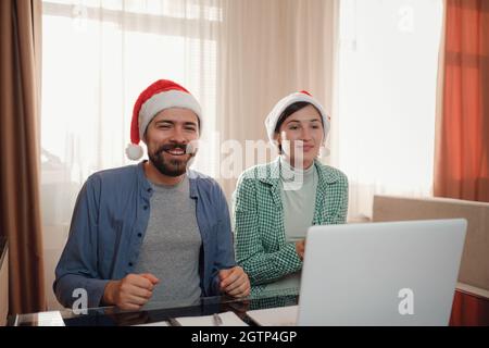 Glückliches junges Paar verwenden oder schauen etwas auf Laptop-pc für weihnachten. Videoanruf feiert virtuelle weihnachten und Neujahr Party zu Hause im Lockdown. internet-Shopping-Konzept Stockfoto