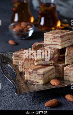 Köstliche Scheiben orientalischer Milch-Halva mit Mandeln und Kakao auf dunkelgrauem Hintergrund. Usbekische traditionelle handgemachte Süßigkeiten. Stockfoto