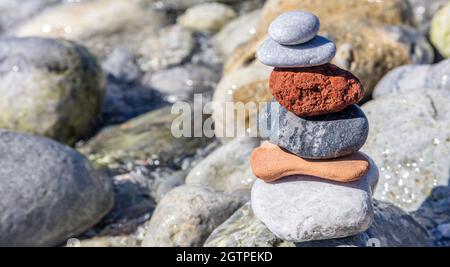 Zen-Balancesteine, glatter Kieselsteinturm auf nassem Felshintergrund, sonniger Tag an der felsigen Küste. Harmonie und Frieden am Meer Stockfoto