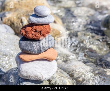 Zen-Balancesteine, glatter Felsturm auf nassem Kiesgrund gestapelt, sonniger Tag an der Küste. Harmonie und Frieden am Meer Stockfoto