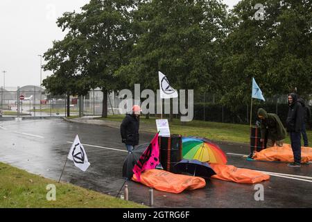 Farnborough, Großbritannien. Oktober 2021. Die Klimaaktivisten der Extinction Rebellion liegen auf der Straße, die in Treibstofffässern gesperrt ist, um eine Zufahrt zum Flughafen Farnborough zu blockieren. Aktivisten blockierten drei Zugänge zum privaten Flughafen, um erhöhte Kohlendioxidwerte hervorzuheben, die von superreichen Passagieren mit privaten Jets und "Greenwashing" vom Flughafen produziert werden, indem sie einen Wechsel zu nachhaltigem Flugkraftstoff (SAF) ankündigten. Kredit: Mark Kerrison/Alamy Live Nachrichten Stockfoto
