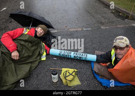 Farnborough, Großbritannien. Oktober 2021. Die Bilder der Klimaaktivisten der Extinction Rebellion werden mit einem Armrohr zusammengeschlossen dargestellt, um einen Eingang zum Flughafen Farnborough zu blockieren. Aktivisten blockierten drei Zugänge zum privaten Flughafen, um erhöhte Kohlendioxidwerte hervorzuheben, die von superreichen Passagieren mit privaten Jets und "Greenwashing" vom Flughafen produziert werden, indem sie einen Wechsel zu nachhaltigem Flugkraftstoff (SAF) ankündigten. Kredit: Mark Kerrison/Alamy Live Nachrichten Stockfoto