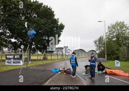 Farnborough, Großbritannien. Oktober 2021. Die Klimaaktivisten der Extinction Rebellion werden auf einem Stahlstativ abgebildet und mit einem Armrohr verriegelt, um einen Eingang zum Flughafen Farnborough zu blockieren. Aktivisten blockierten drei Zugänge zum privaten Flughafen, um erhöhte Kohlendioxidwerte hervorzuheben, die von superreichen Passagieren mit privaten Jets und "Greenwashing" vom Flughafen produziert werden, indem sie einen Wechsel zu nachhaltigem Flugkraftstoff (SAF) ankündigten. Kredit: Mark Kerrison/Alamy Live Nachrichten Stockfoto