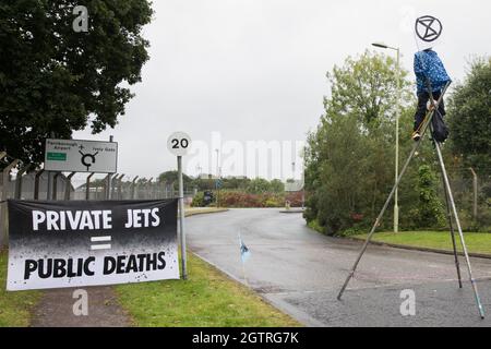 Farnborough, Großbritannien. Oktober 2021. Ein Klimaaktivist des Extinction Rebellion ist auf einem Stahlstativ befestigt, um den Eingang zum Flughafen Farnborough zu blockieren. Aktivisten blockierten drei Zugänge zum privaten Flughafen, um erhöhte Kohlendioxidwerte hervorzuheben, die von superreichen Passagieren mit privaten Jets und "Greenwashing" vom Flughafen produziert werden, indem sie einen Wechsel zu nachhaltigem Flugkraftstoff (SAF) ankündigten. Kredit: Mark Kerrison/Alamy Live Nachrichten Stockfoto