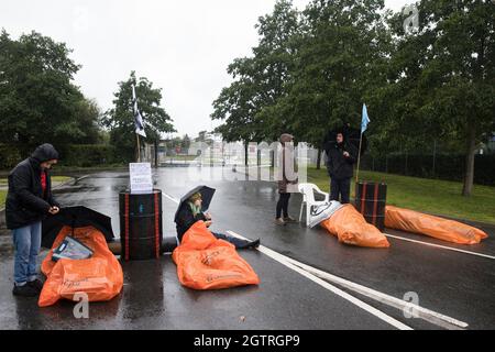 Farnborough, Großbritannien. Oktober 2021. Die Klimaaktivisten des Extinction Rebellion liegen auf der Straße, die für Treibstofffässer gesperrt ist, um den Zugang zum Flughafen Farnborough zu blockieren. Die Aktivisten blockierten drei Zugänge zum privaten Flughafen, um erhöhte Kohlendioxidwerte hervorzuheben, die von superreichen Passagieren mit Privatjets und "Greenwashing" vom Flughafen produziert werden, indem sie einen Wechsel zu nachhaltigem Flugkraftstoff (SAF) ankündigten. Kredit: Mark Kerrison/Alamy Live Nachrichten Stockfoto