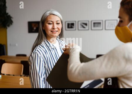 Zwei Angestellte, die in sozialer Distanz stehen und eine Gesichtsmaske tragen und im Büro sprechen Stockfoto
