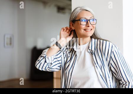Glückliche weißhaarige reife Frau in Brillen lächelnd und schaut nach draußen Stockfoto