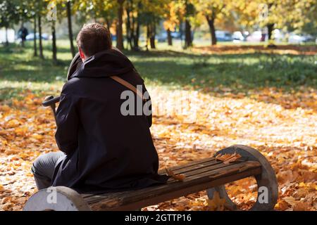 Glücklicher junger Vater mit Kinderwagen sitzt auf der Bank in der Natur im Park Stockfoto