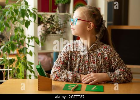 Ein schönes Mädchen mit Down-Syndrom ist in der Klasse beschäftigt und studiert Zahlen Stockfoto