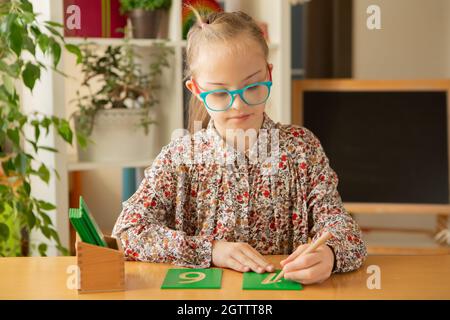 Ein schönes Mädchen mit Down-Syndrom ist in der Klasse beschäftigt und studiert Zahlen Stockfoto