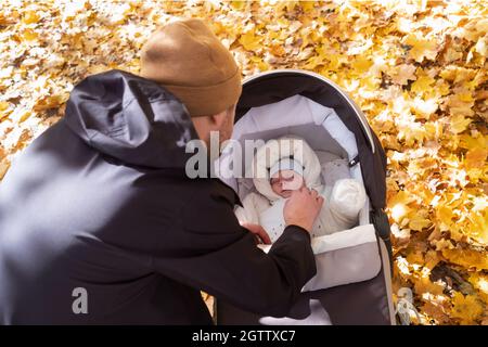 Glücklicher junger Vater mit Kinderwagen sitzt auf der Bank in der Natur im Park Stockfoto