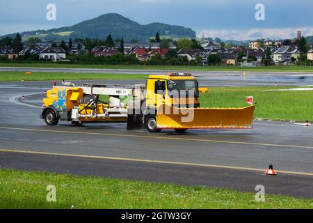 Salzburg, Österreich - 20. Mai 2013: Reinigung der Flughafenpiste. Flugplatz Beton und Asphalt Oberflächenreiniger. Schneepflug. Schnee- und Schmutzentfernung Traktor vehi Stockfoto