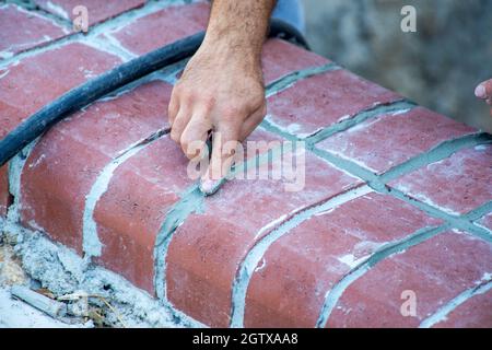 Die Hand eines Handwerkers füllt die Fugen zwischen den Ziegeln mit dem Finger Stockfoto