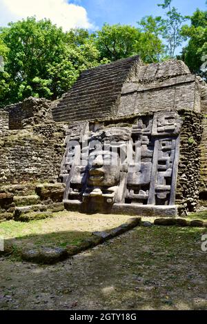 Blick auf eine der beiden geschnitzten Steinmasken auf dem Maskentempel in Lamanai mit einem Teil des Tempels in Sicht. Stockfoto