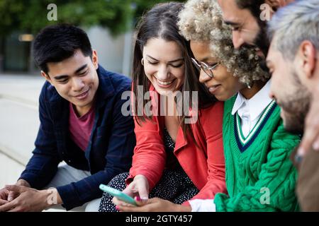 Eine Gruppe junger Menschen, die Spaß haben, während sie sich Videoinhalte auf dem Mobiltelefon ansehen Stockfoto