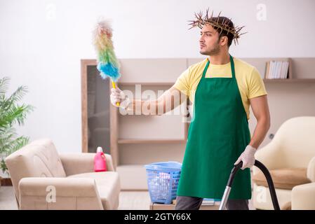 Junger männlicher Auftragnehmer, der auf dem Kopf einen stacheligen Kranz trägt und Hausarbeit leistet Stockfoto