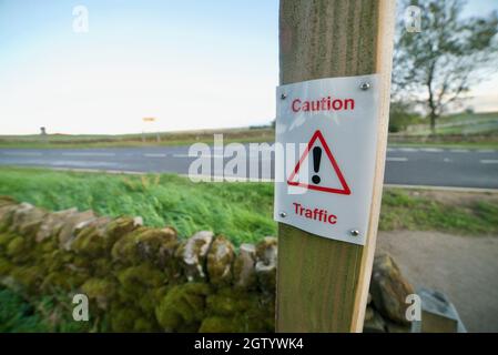 Achtung Verkehr – kleines Warnschild neben einer Landstraße für Fußgänger, Ausrufezeichen in rotem Dreieck. Stockfoto