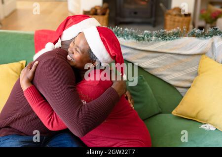 Glückliches afroamerikanisches Seniorenpaar, das sich zur weihnachtszeit auf dem Sofa umarmt Stockfoto