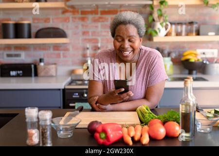 Glückliche afroamerikanische ältere Frau mit Smartphone-IT-Küche Stockfoto