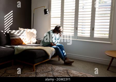Müde afroamerikanische ältere Frau, die zu Hause auf dem Bett sitzt Stockfoto