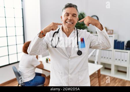 Arzt mittleren Alters Mann in der Klinik mit einem Patienten lächelnd fröhlich zeigen und zeigen mit den Fingern Zähne und Mund. Zahngesundheit Konzept. Stockfoto