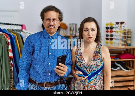 Interrassisches Paar im mittleren Alter im Einzelhandel mit Smartphone skeptisch und nervös, runzelte die Stirn wegen des Problems. Negative Person. Stockfoto