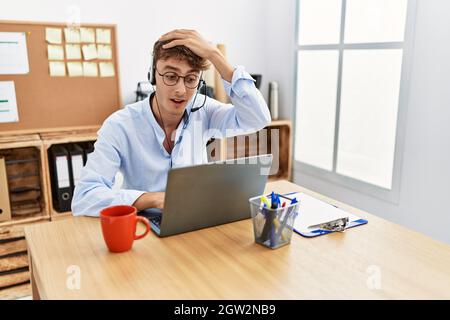 Der junge kaukasische Mann, der im Büro ein Headset für Callcenter-Agenten trug, war gestresst und frustriert, mit der Hand am Kopf, überrascht und wütend Stockfoto