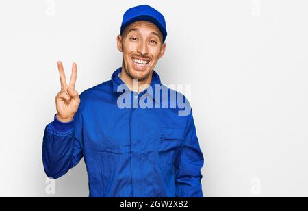 Glatze Mann mit Bart tragen Baumeister Jumpsuit Uniform zeigt und zeigt mit den Fingern Nummer zwei, während lächelnd zuversichtlich und glücklich. Stockfoto