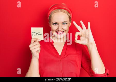 Junge blonde Frau hält unendliche Symbol Erinnerung tun ok Zeichen mit den Fingern, lächelnd freundlich gestikulieren ausgezeichnete Symbol Stockfoto