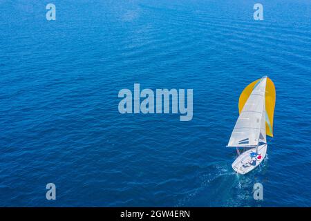 Sommerurlaub auf dem Wasser. Luftaufnahme einer schönen weißen Segelyacht mit einem farbigen Segel. Stockfoto