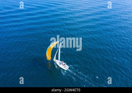 Sommerurlaub auf dem Wasser. Luftaufnahme einer schönen weißen Segelyacht mit einem farbigen Segel. Stockfoto