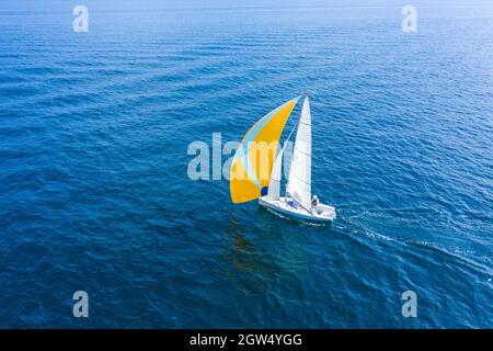 Sommerurlaub auf dem Wasser. Luftaufnahme einer schönen weißen Segelyacht mit einem farbigen Segel. Stockfoto