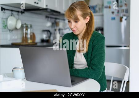 Fokussierte Frau, die aus der Küche auf einem Laptop arbeitet. Konzept von Home Office und Multitasking Stockfoto