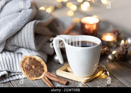 Gemütliches Zuhause Winter Komposition mit einer Tasse Tee auf einem verschwommenen Hintergrund mit brennenden Kerzen und Bokeh Lichter und gestrickte Elemente. Stockfoto