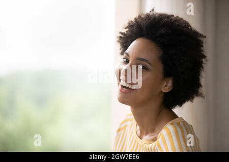 Junge afroamerikanische Frau, die lachend neben dem Fenster steht. Stockfoto
