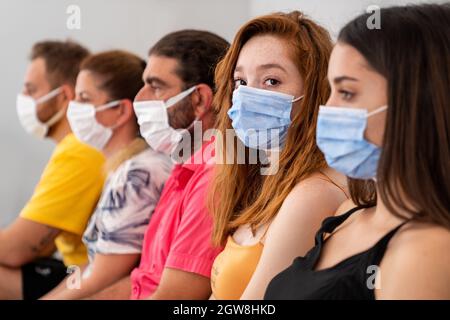 Gruppe von Menschen sitzt und wartet in einem Saal mit schützender Gesichtsmaske in sozialer Distanz. Pandemie und Gesundheitskonzept. Hochwertige Fotos Stockfoto