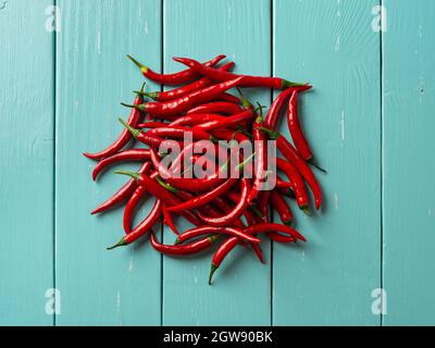 Ein paar rote, scharfe Chilischoten auf einem türkisfarbenen Holztisch. Ganze frische, scharfe Chilischoten auf der Tischplatte. Ein paar rohe Bio-Chilischoten aus der Draufsicht. Stockfoto