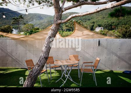 Gemütlicher Picknicktisch und Stühle unter einem Baldachin an einem Baum auf einem Hintergrund von Bergen befestigt. Stockfoto