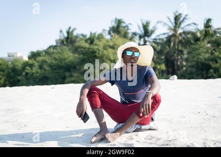Afrikanischer Mann, der am Sandstrand sitzt Stockfoto