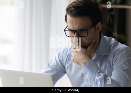 Nahaufnahme eines durchdachten Mannes in einer Brille, der auf den Laptop-Bildschirm blickt Stockfoto