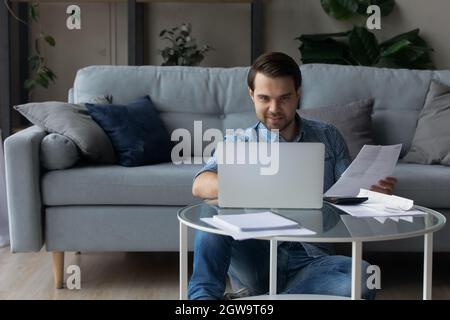 Lächelnder Mann, der zu Hause mit einem Laptop Hausrechnungen berechnet Stockfoto
