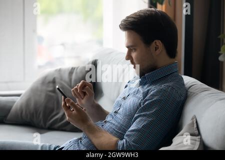Seitenansicht fokussierter Mann mit Smartphone, sitzend auf Couch Stockfoto