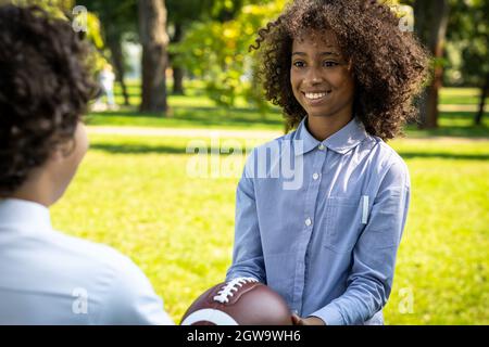 Filmisches Bild einer Familie aus den emiraten, die Zeit im Park verbringt. Bruder und Schwester spielen Fußball im Gras Stockfoto