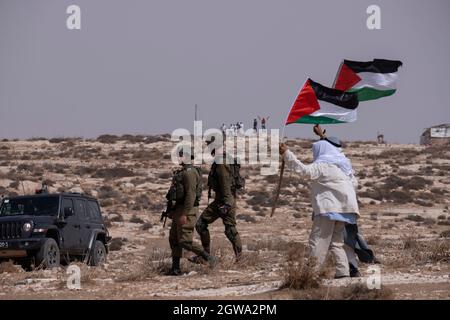 Palästinensische Demonstranten halten die palästinensische Fahne auf dem Weg mit israelischen Soldaten während einer Demonstration gegen die Abschneidung der Wasserversorgung für palästinensische Dörfer, Und Solidarität mit dem palästinensischen Hirtenlager Khirbat al-Mufaqara, das Anfang dieser Woche von jüdischen Siedlern in den Südhebron-Bergen am 02. Oktober 2021 im Westjordanland, Israel, angegriffen wurde. Seit zwei Jahrzehnten versuchen die israelischen Behörden, Palästinenser, die in der Region South Hebron Hills leben, zu vertreiben, weil sie illegal in israelischen militärischen Feuerzonen leben. Stockfoto