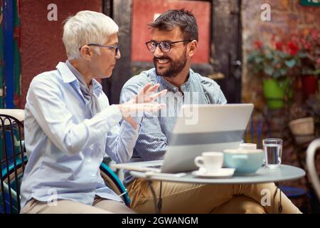 Ältere kaukasische Frau erklärt einem jungen erwachsenen bärtigen Mann etwas mit Handgesten Stockfoto