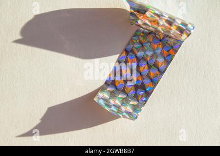 Ein Stück holographische Folie auf weißem Hintergrund, harte Schatten von der Folie. Draufsicht. Zu kopierende Position. Stockfoto
