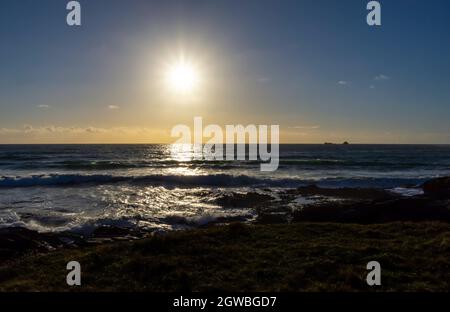 Ein gelbes Leuchten am Himmel, wenn die Sonne über dem Atlantischen Ozean untergeht, was schöne Reflexionen auf dem Wasser verursacht, wenn der Herbst naht. Sonnenstrahlen können in gesehen werden Stockfoto