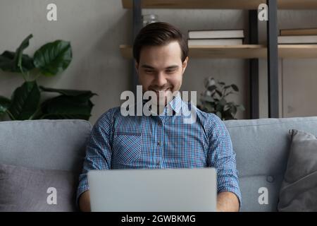 Lächelnder Mann mit Laptop, der zu Hause auf der Couch sitzt Stockfoto