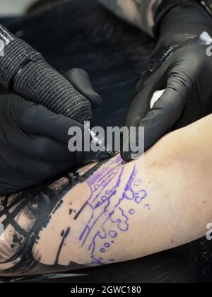 Eine vertikale Nahaufnahme eines Tätowierers mit schwarzen Handschuhen, der eine Tätowierung auf dem Arm einer Person tätowiert Stockfoto